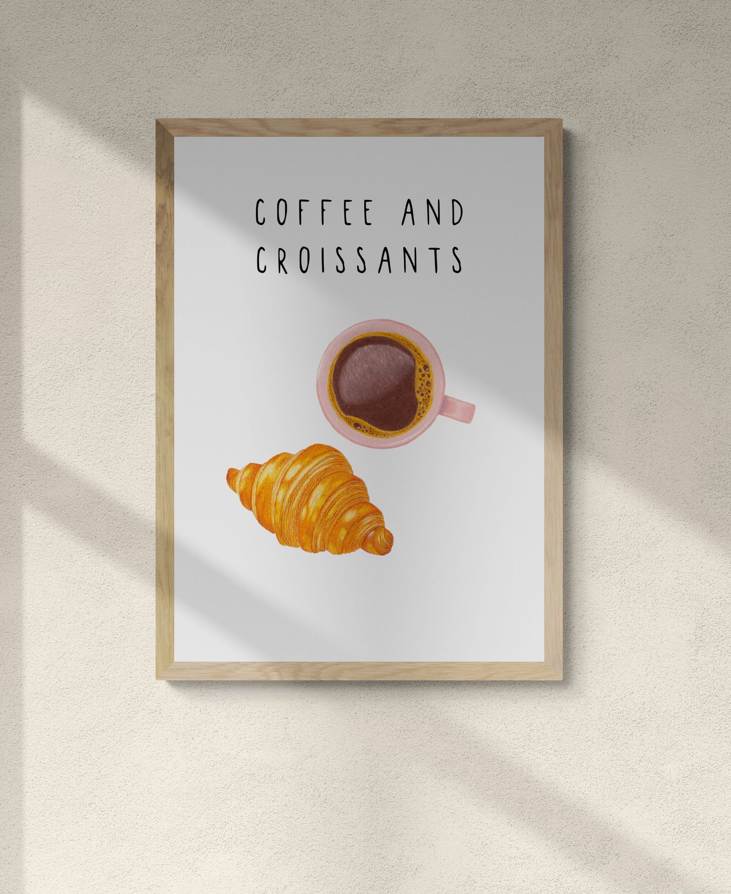 Framed artwork with a cup of coffee and croissant illustration on a light background and the words 'coffee and croissants' at the top of the print