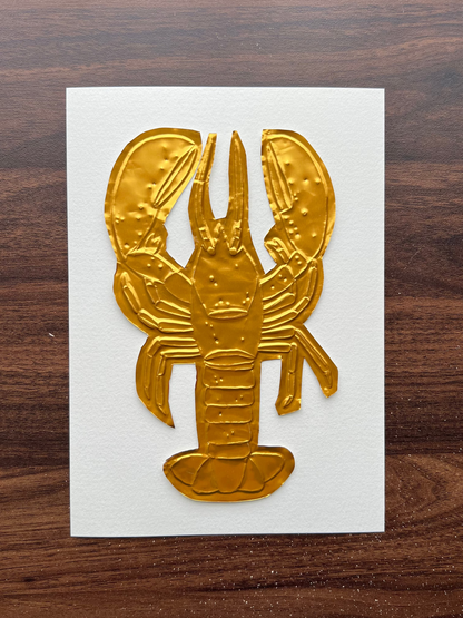 A gold lobster-shaped metallic embellishment on a white A5 rectangular card