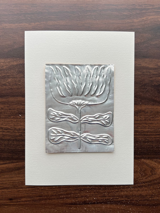 A square silver metal embossing of a flower design, mounted on a white A5 card 